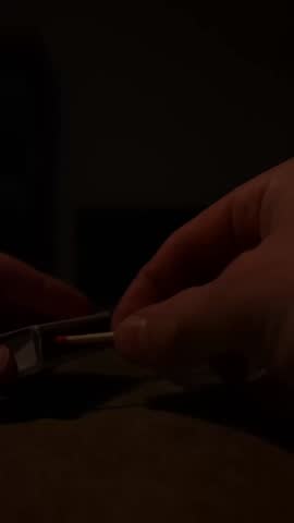Vertical close-up shows a hand striking and holding a burning match as a small flame ignites