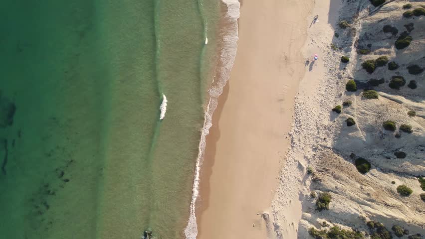 Cinematic overhead drone shot of the crystal clear Atlantic water and golden sand beach along the coastline of Sagres, Algarve, Portugal.
