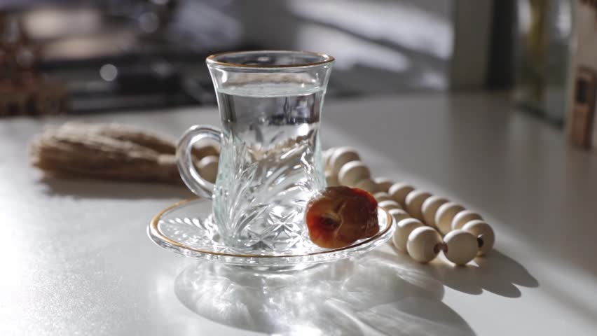 On the white table there is a glass of water, a date and a rosary.