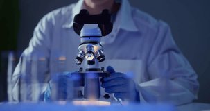 Scientist adjusts microscope objectives and focuses under blue laboratory lighting, gloved hands rotating lenses and peering closely at samples. - Powered by Shutterstock - Get 15% off with code: PIKWIZARD15