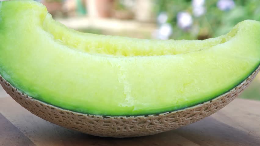 close up of a green cantaloupe slice on a piece of wooden.