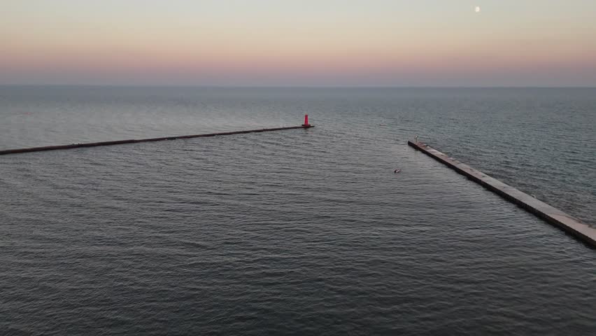 Aerial of Sheboygan Wisconsin USA at dusk on the shore of Lake Michigan.  Early Fall evening, slow approach shot of lighthouse under moonlight.