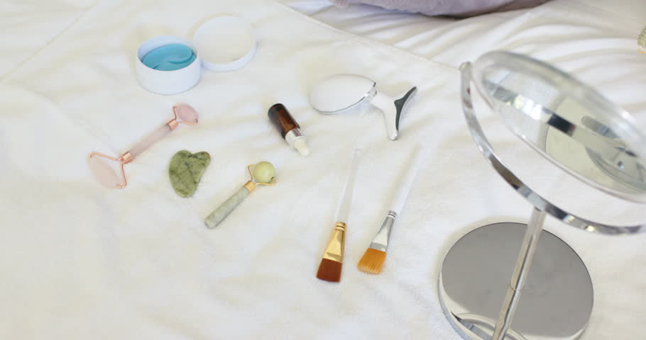 Camera slowly tightening frame, showcasing rollers, gua sha, brushes, mirror, highlighting details. Flatlay, skincare, vanity, jade, rose-gold, minimalist, serene
