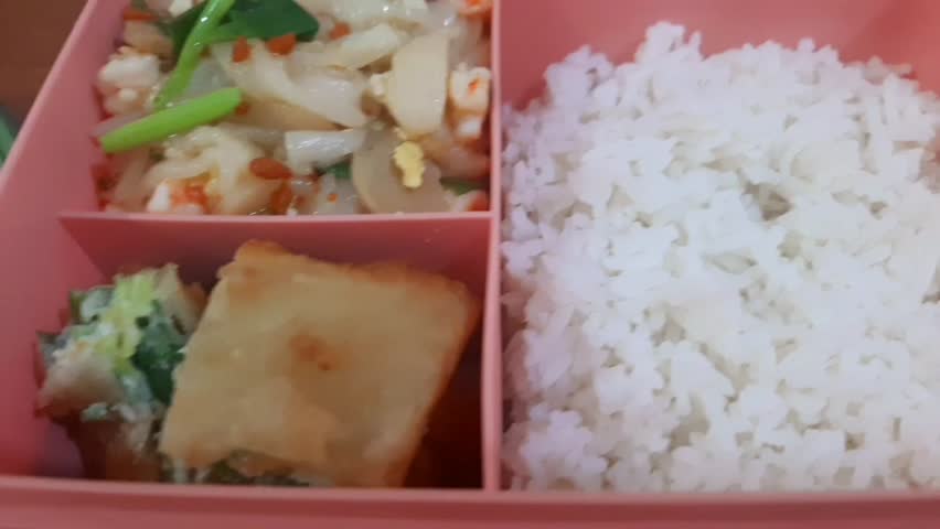 A lunch box filled with rice, fried kwetiau noodles, sliced meatballs, vegetables, and fried egg martabak. Homemade Indonesian meal packed in a food container, representing traditional Asian cuisine and daily homemade lunch concept