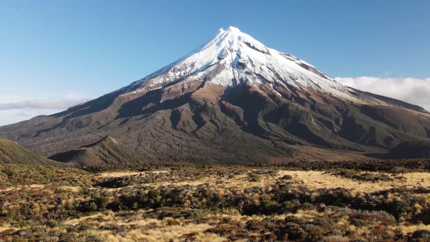 Taranaki, New Zealand. Drone crane of volcano mountain with snow capped peak, sunny day.