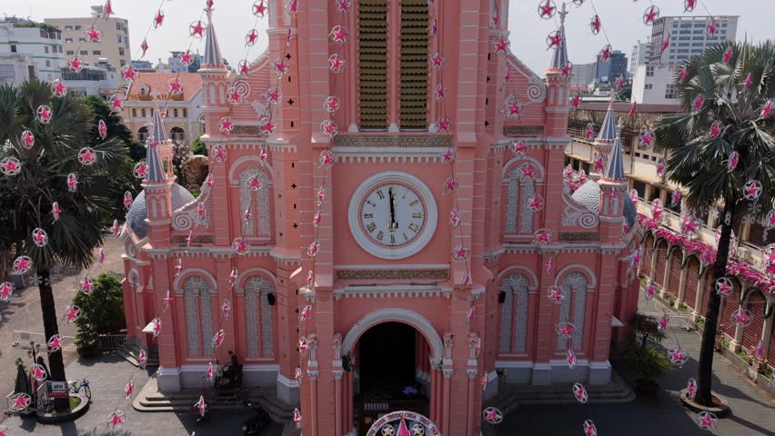 Aerial drone view of the iconic pink church in Ho Chi Minh City, Vietnam. Historic cathedral architecture surrounded by dense urban skyline and modern city buildings.