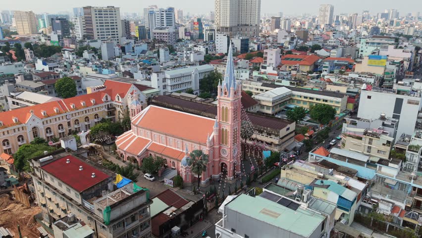 Cinematic aerial view of Tan Dinh Pink Church in Ho Chi Minh City, Vietnam. Iconic pink cathedral surrounded by urban skyline and dense city architecture in Southeast Asia.
