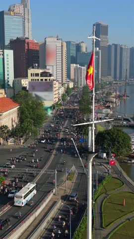 Aerial view of Vietnamese flag above busy traffic in Ho Chi Minh City. Saigon River and modern skyline in District 1, Vietnam economic center.
