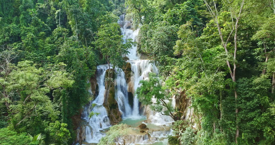 An aerial view of Tat Kuang Si Falls reveals its breathtaking multi-tiered cascades flowing into vivid turquoise pools, surrounded by dense tropical jungle in northern Laos.
