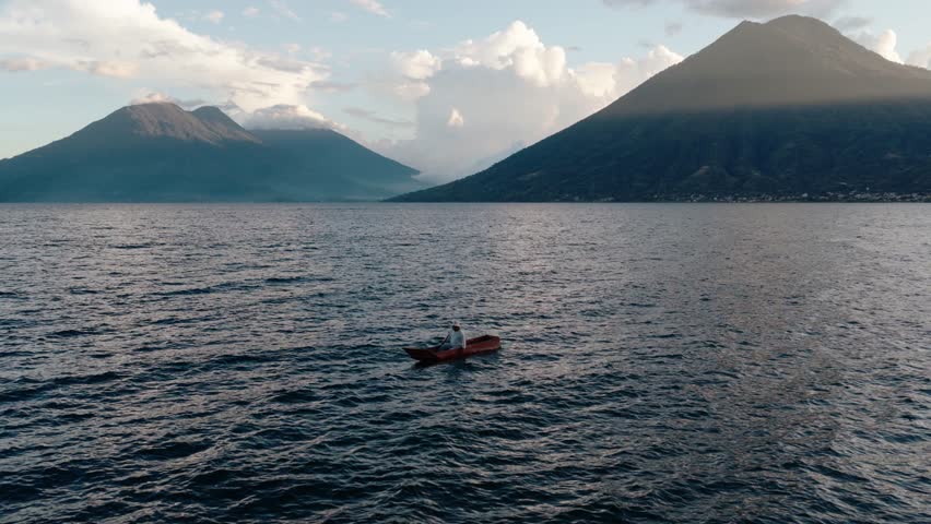 A lone canoe crosses Lake Atitlan framed by volcanic mountains in Guatemala
