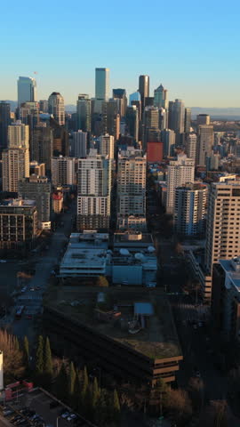 Aerial cityscape of Seattle Washington downtown with modern skyscrapers, residential towers and Puget Sound coastline during golden hour, showing urban density and calm evening light.