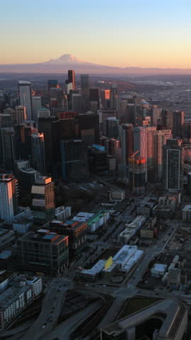 Aerial panorama of Seattle Washington skyline with Mount Rainier on the horizon at sunset, revealing dense urban core, modern high rises and expansive coastal waterways.