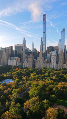 Cinematic aerial view of Central Park surrounded by Manhattan skyline in New York City New York with autumn trees modern skyscrapers and clear sky creating a breathtaking urban landscape.