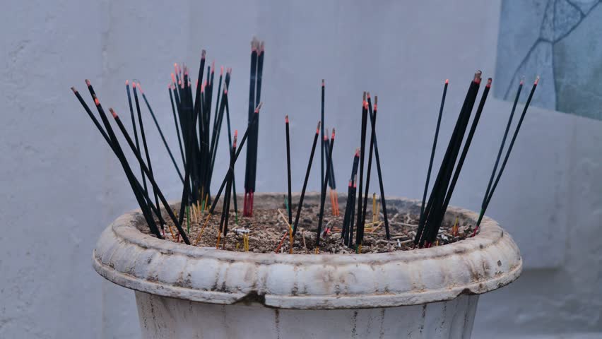 Burning incense sticks in white ceramic pot with glowing red embers and rising smoke during Buddhist prayer ritual, spiritual meditation and religious ceremony concept
