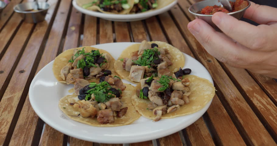 Hands Spooning Salsa onto Traditional Mexican Street Tacos, close-up
