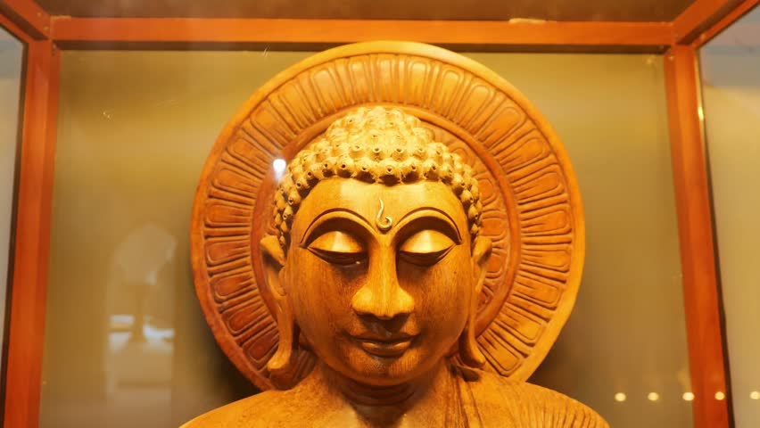 Wooden Buddha statue face with closed eyes and halo backdrop, detailed carved sculpture in glass display, spirituality and meditation concept
