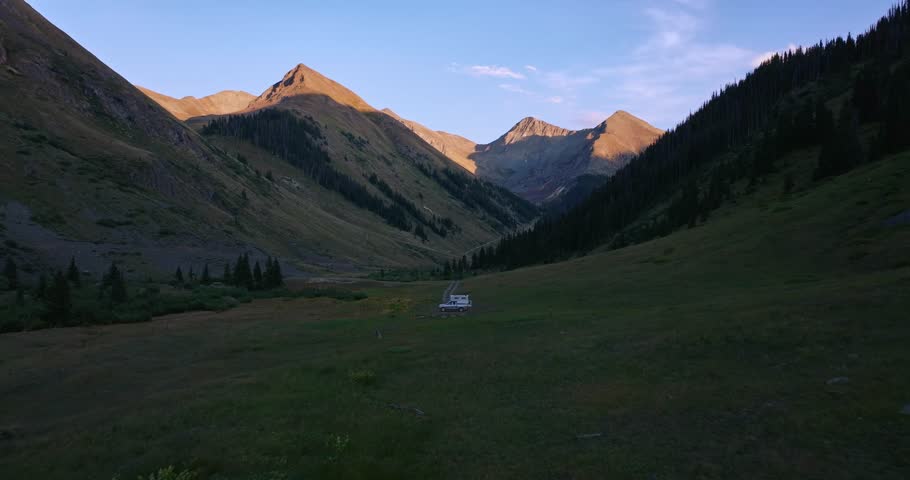 Golden hour aerial of alpine valley with dirt road and camper at dusk, alpenglow, Trans America Trail, Colorado, USA