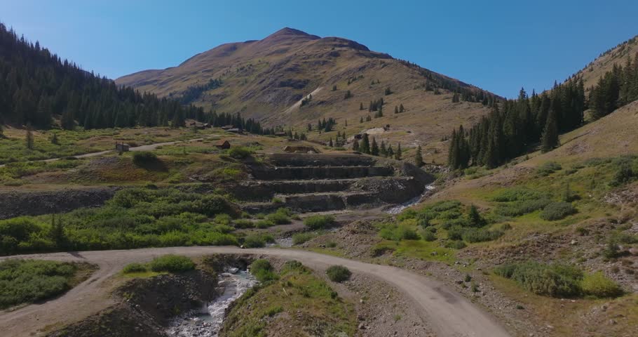 Closer aerial of historic mining terraces and flowing creek in alpine valley