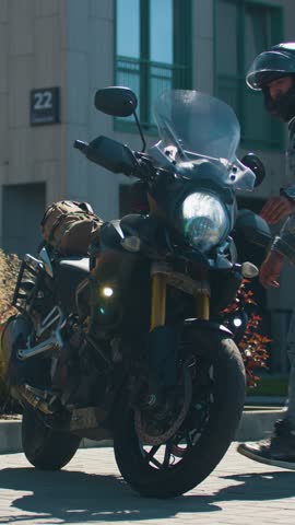 Vertical footage of a biker rides his motorcycle through the parking lot. He approaches the camera and passes by. The motorcyclist confidently rides his motorcycle and embarks on an adventure.