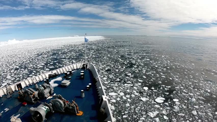 Ship navigating through icy waters of the Southern Ocean under a bright blue sky near the frozen landscapes of Antarctica.