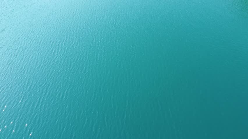 Clear blue lake surrounded by green forest and rocky shoreline in a peaceful natural setting.