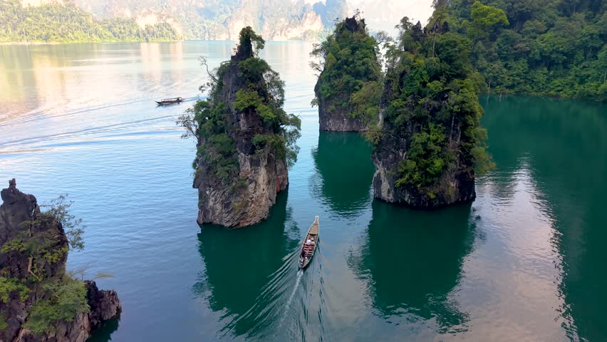 Experience the stunning beauty of Khao Sok National Park in Thailand as boats glide past massive limestone cliffs and vibrant greenery. This tranquil landscape invites adventure and relaxation.