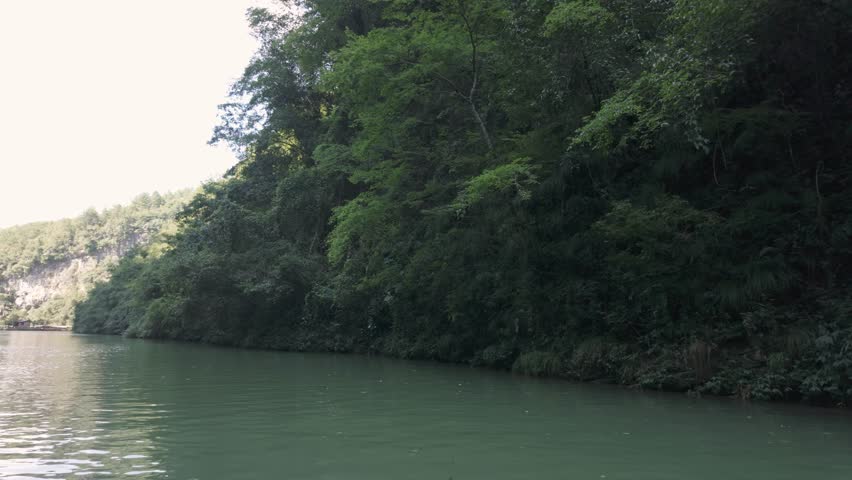 A tranquil boat ride through the lush Zhangjiajie Grand Canyon in China, showcasing steep forested cliffs and emerald green water. Perfect for travel documentaries and nature exploration content.