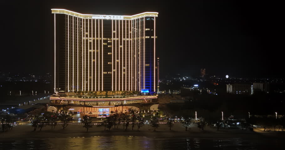 Panning aerial view of an illuminated luxury hotel on a beach in Sihanoukville.