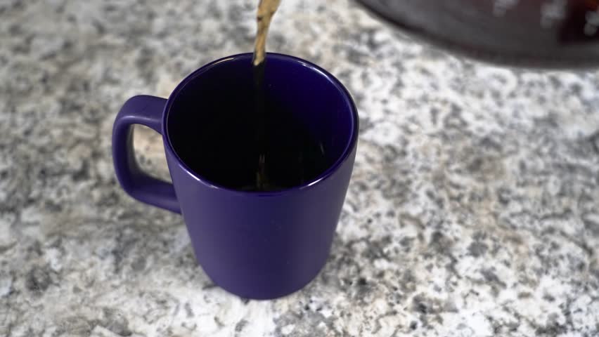 Freshly brewed coffee pouring into a purple mug on a granite countertop. Cream is added, mixing into the hot beverage, and a hand lifts the cup