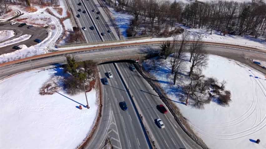 Aerial view of an overpass on the Southern State Parkway on a sunny day with snow on the ground. The camera tilted down dolly in, pan left, dolly out and tilt up as vehicles drive by, winter scenery.