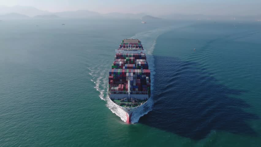 Aerial front view of a massive cargo container ship cruising through deep blue ocean waters during the day