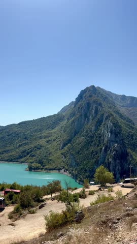 Panoramic view of Lake Bovilla (Liqeni i Bovillës) in Albania, featuring turquoise water surrounded by lush green hills and layered mountain ranges under a clear blue sky. Scenic summer landscape near Tirana, perfect for travel and nature themes.