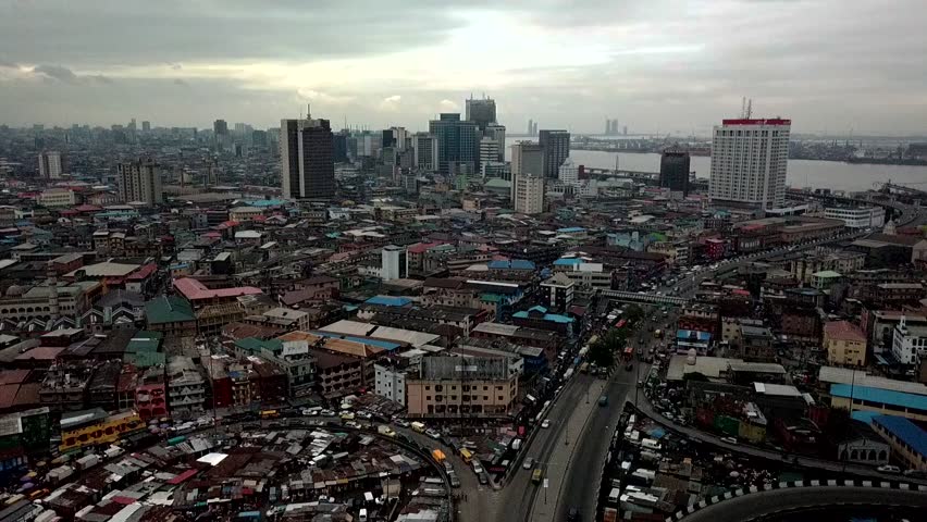 Aerial view of Lagos Island, Nigeria, showing dense urban rooftops, busy roads and high-rise skyline near Lagos Lagoon under cloudy skies—West African megacity cityscape.