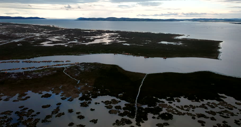 Uros floating reed islands on Lake Titicaca near Puno, Peru, showing wetlands, channels and the wide high-altitude lake under soft evening light, cinematic aerial view