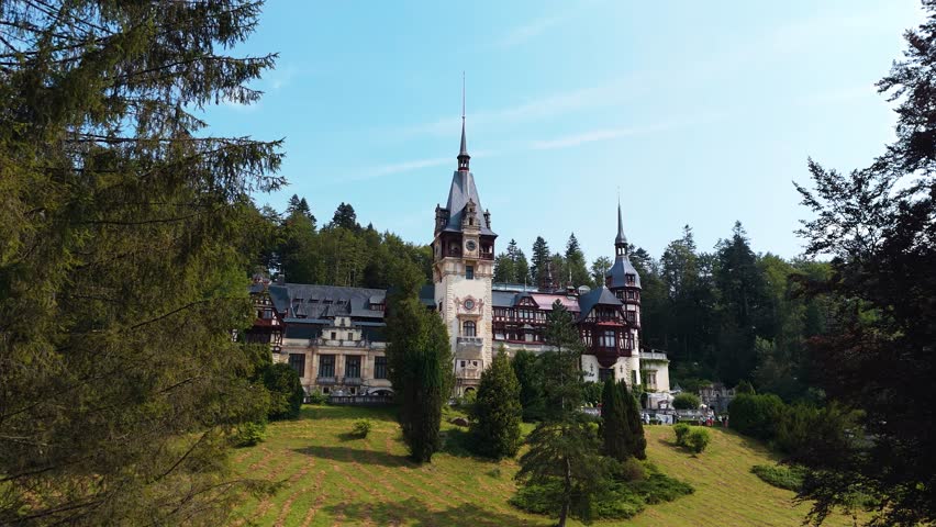 Drone flies toward Peleș Castle surrounded by dense mountain forest