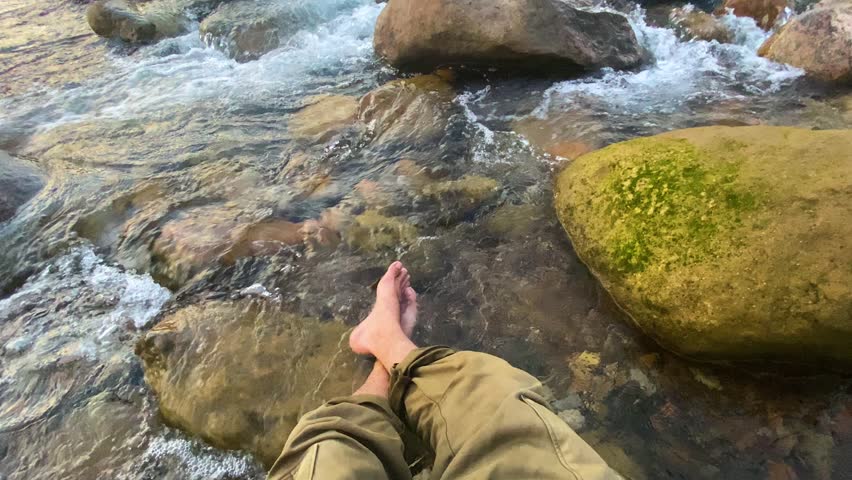 Moment of relaxation with a person bare feet immersed in the clear cool water of a rocky river