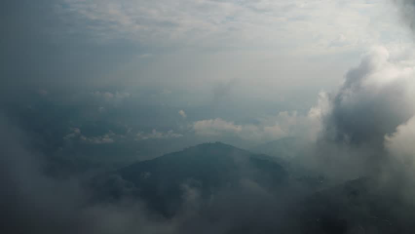 Dramatic cloud movement showing distant Himalayan mountain peaks above forests and foothills. Nepal