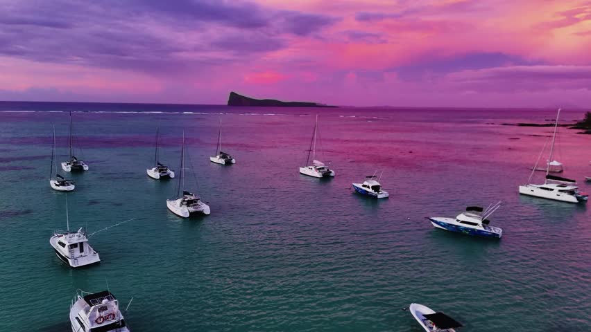 Anchored boats in a tropical lagoon captured during a vivid red sunset in Mauritius. Calm waters and a colorful sky create a serene island atmosphere, an aerial shot.
