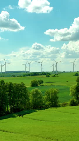 Vertical shot of a wind farm on lush green hills under a bright blue sky with fluffy clouds. Ideal for renewable energy and sustainability content.