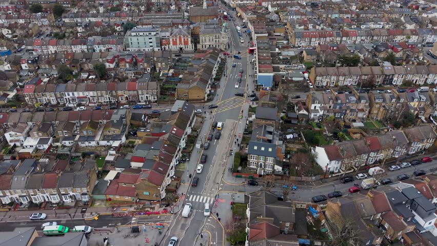 Leyton High Road drone flyover toward Leyton Town Hall, showing traffic flow, road markings, yellow box junction, and a red double-decker bus driving away in London, UK.