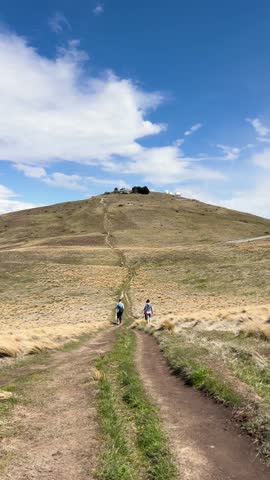 Hikers ascend Mount John Track under blue skies in Lake Tekapo, New Zealand