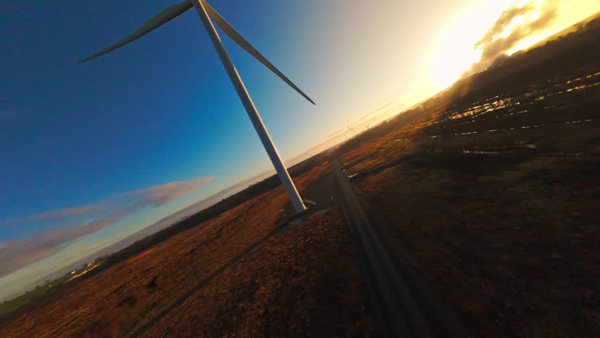 Immersive FPV drone orbit around wind turbine towers during sunrise. Dynamic aerial motion combined with warm sunlight creates an epic renewable energy scene in rural Ireland.
