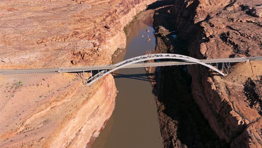This high-altitude drone shot emphasizes the architectural symmetry of the bridge as it crosses the Colorado River. Long shadows and red rock textures create a dramatic desert scene in 4K.