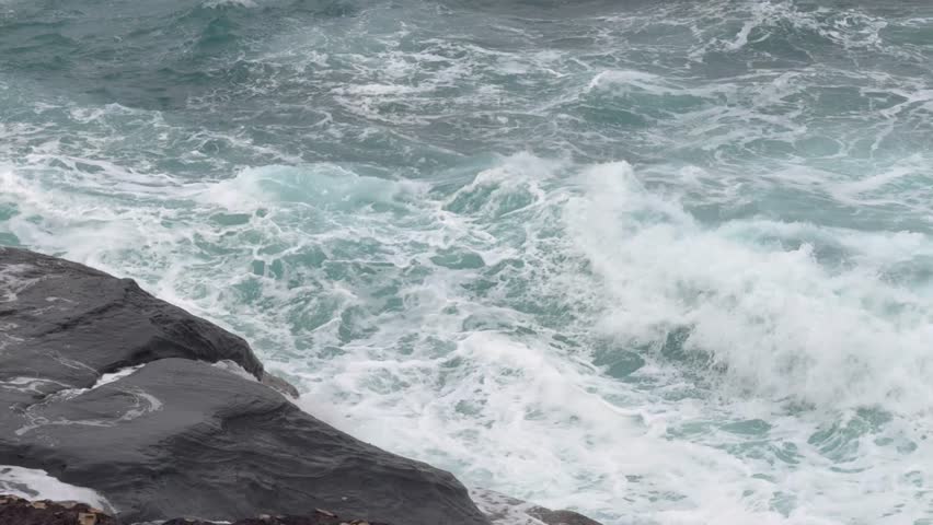 Ocean waves crashing against a rocky shoreline, creating white foam.