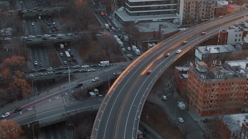 Cars move along the highway in New York City as the sun sets. The scene shows busy roads and buildings near the highway in the evening light.