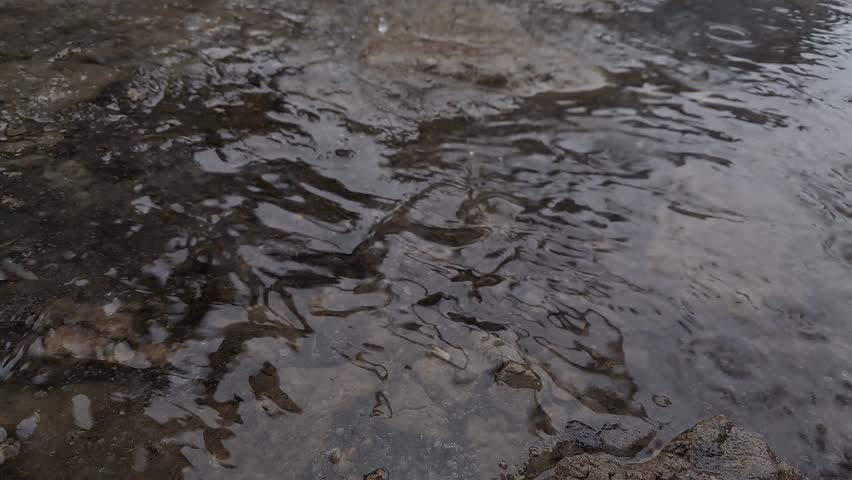 Close up of raindrops hitting the surface of a water stream and puddle on the ground. Ripples and splashes during a storm. 4K UHD 30fps.