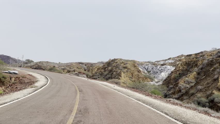 Curved asphalt road through rocky hills under overcast sky
Empty winding road curving through rugged rocky hills and dry landscape, scenic travel route with leading lines and cloudy sky.