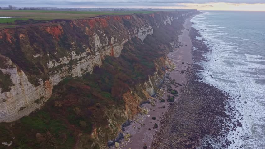 White chalk cliffs with eroded faces, vegetation cover, and a long pebble beach beside the English Channel at Plage de Saint-Jouin-Bruneval, Normandy, France, drone pulling out