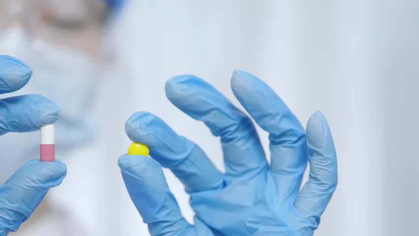 A faceless doctor with gloves holding colorful vibrant white pink and yellow drug pill capsule, medication in various shapes and sizes for health treatment and drug care concepts