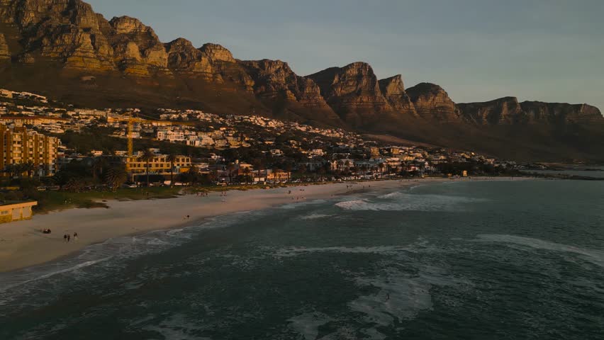 Smooth low altitude aerial drone footage flying towards Camps Bay in Cape Town South Africa during sunset capturing golden light over the coastline